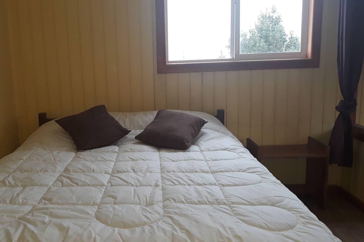 Un lit recouvert d’une courtepointe blanche matelassée et agrémenté de deux oreillers foncés.