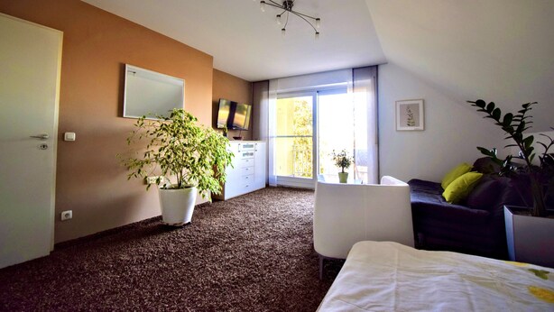 Une chambre à coucher moderne avec une grande fenêtre, un ventilateur de plafond, un lit, un bureau et une plante en pot.