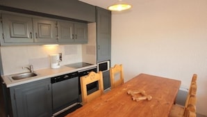 A kitchen with grey cabinets, a wooden dining table, and a hanging light fixture. - Cozy apartment in Les Saisies - 6 pers, fireplace, south balcony (Les Saisies)