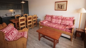 A cozy living room with a sofa, wooden chairs, a coffee table, and a kitchen area in the background. - Cozy apartment in Les Saisies - 6 pers, fireplace, south balcony (Les Saisies)