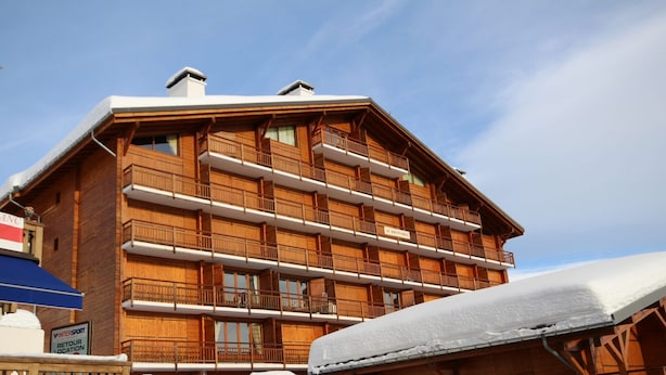 A multi-story wooden building with balconies, likely a hotel or lodge, featuring a sign for "INTERSPORT" and a "RETOUR LOCATION" sign. - Cozy apartment in Les Saisies - 6 pers, fireplace, south balcony (Les Saisies)
