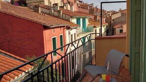 A balcony with a chair and table, overlooking a residential area with terracotta roofs and colorful buildings. - 4EGA41 - Superb F3 in the city center (COLLIOURE)