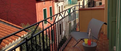 Een balkon met een stoel en tafel, met uitzicht op een woongebied met terracotta daken en kleurrijke gebouwen.