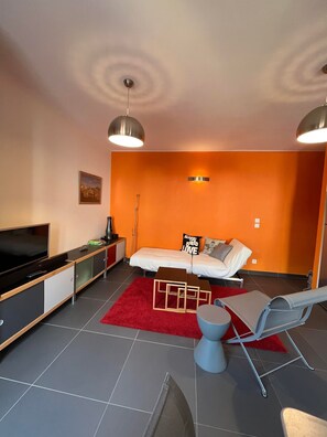 A modern living room with a flat-screen TV, a sofa, a red rug, and a blue chair.