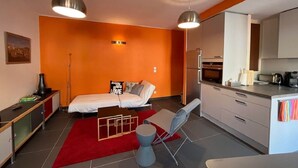 A compact room with a bed, a desk, a chair, a kitchenette, and a red rug. - 4EGA41 - Superb F3 in the city center (COLLIOURE)
