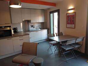 A modern kitchen with white cabinets, a stainless steel oven, and a dining area with a table and chairs.