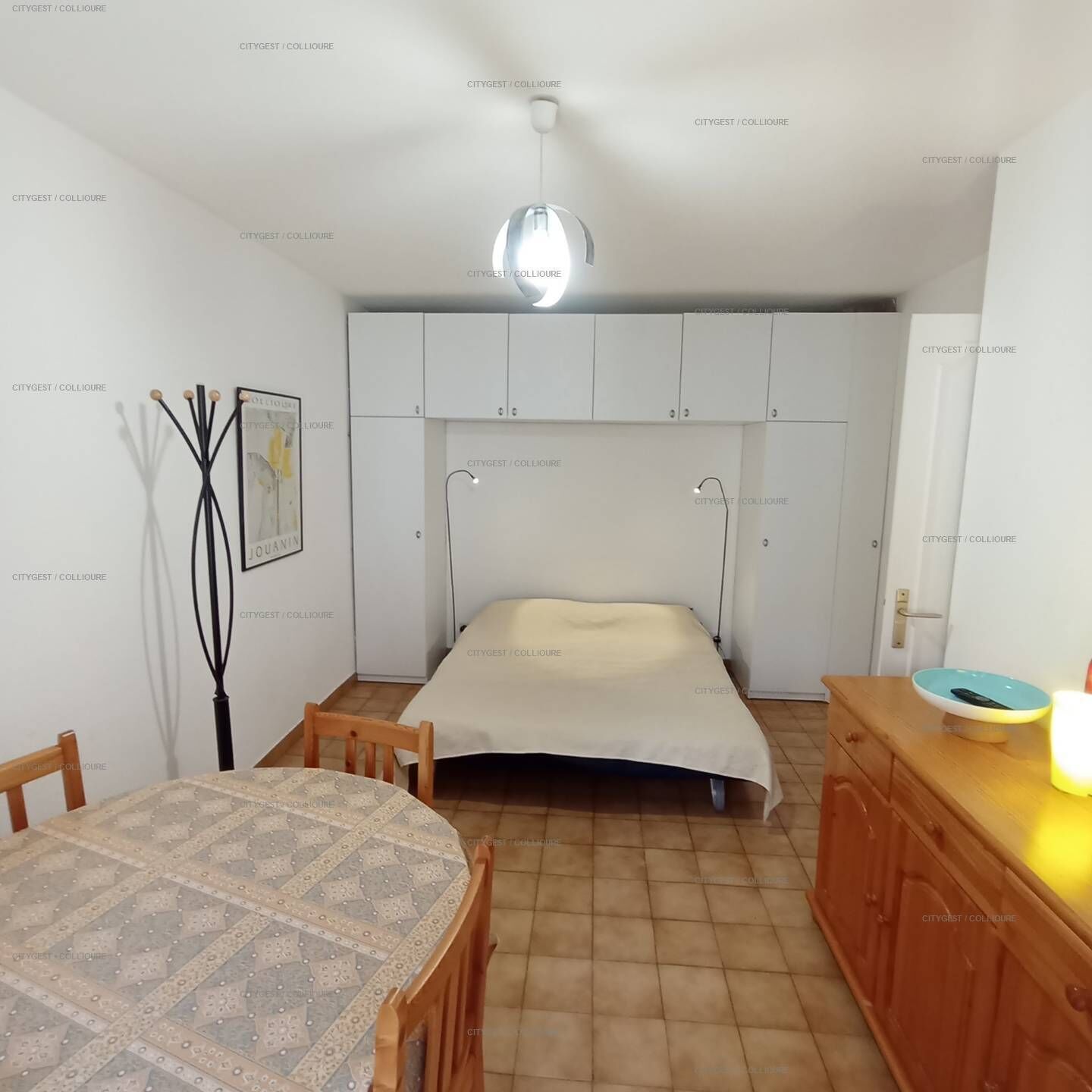 A compact room with a bed, a table, and a cabinet.