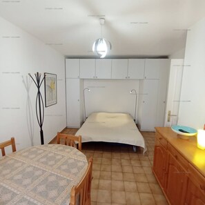 A compact room with a bed, a table, and a cabinet.
