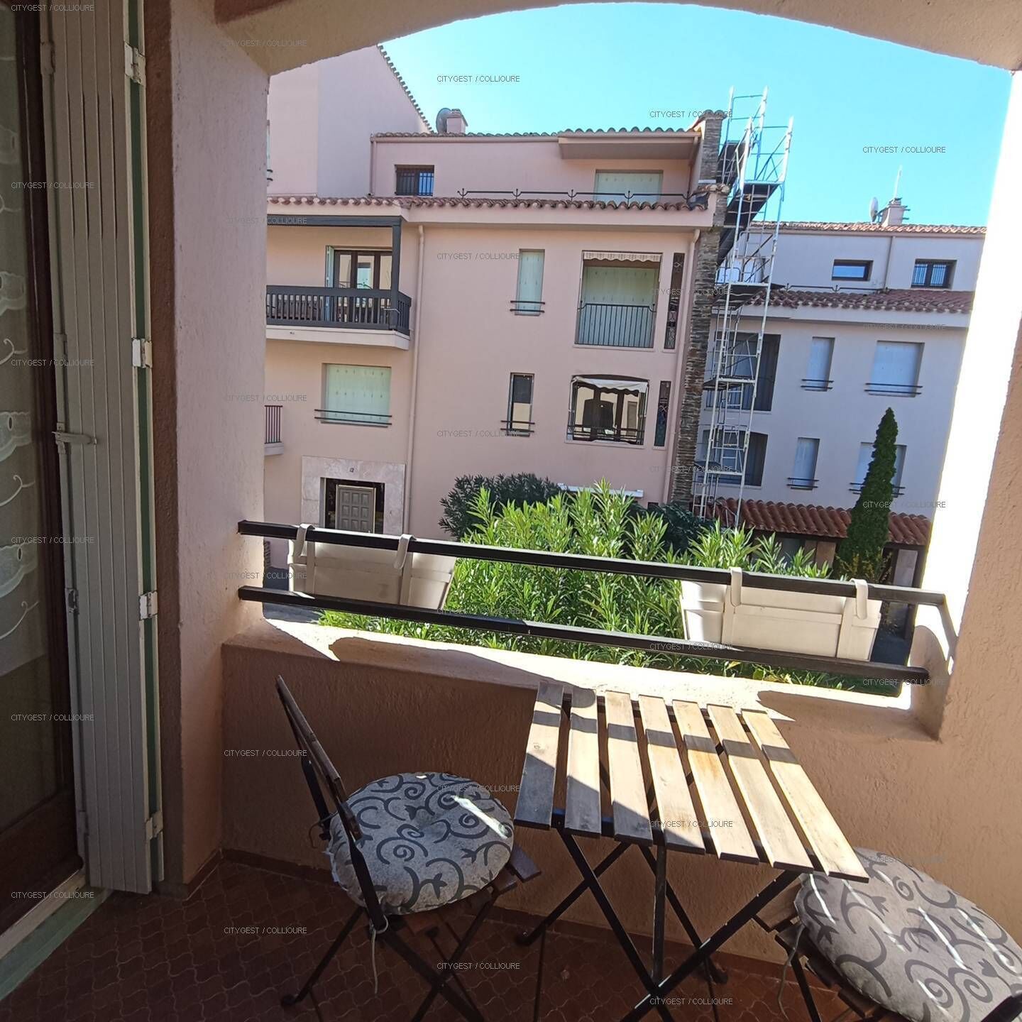 Ein Balkon mit Stuhl und Tisch, mit Blick auf eine Wohngegend und mehrere Gebäude.