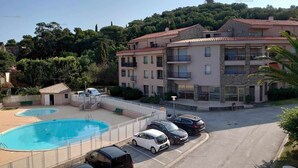 Un edificio residencial de varios pisos con piscina, coches aparcados y un paisaje montañoso al fondo.