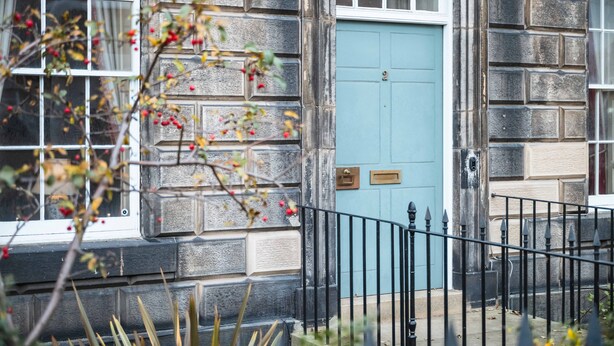 A stone building with a blue door, a window, and a black metal fence.