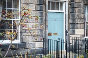 A stone building with a blue door, a window, and a black metal fence.