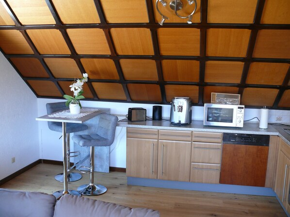 A compact kitchen with a wooden ceiling, a small dining table with a chair, a microwave, a toaster, and a coffee maker. - 2 rooms, kitchen, bathroom (full equipment), terrace (Weiskirchen)