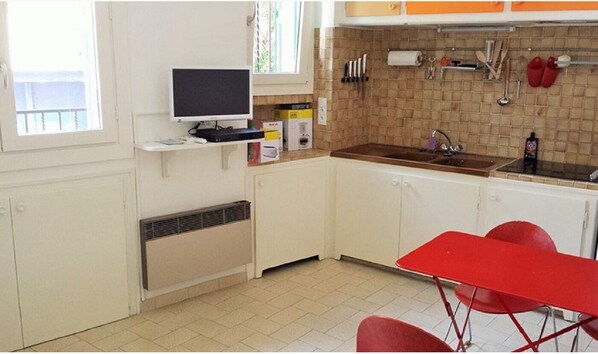 A kitchen with a sink, a television on a shelf, and a red table. - 2EGA41 - Nice studio in historic center (Collioure)
