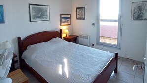 Et soveværelse med seng, natbord, lampe, ventilator og et vindue med udsigt.