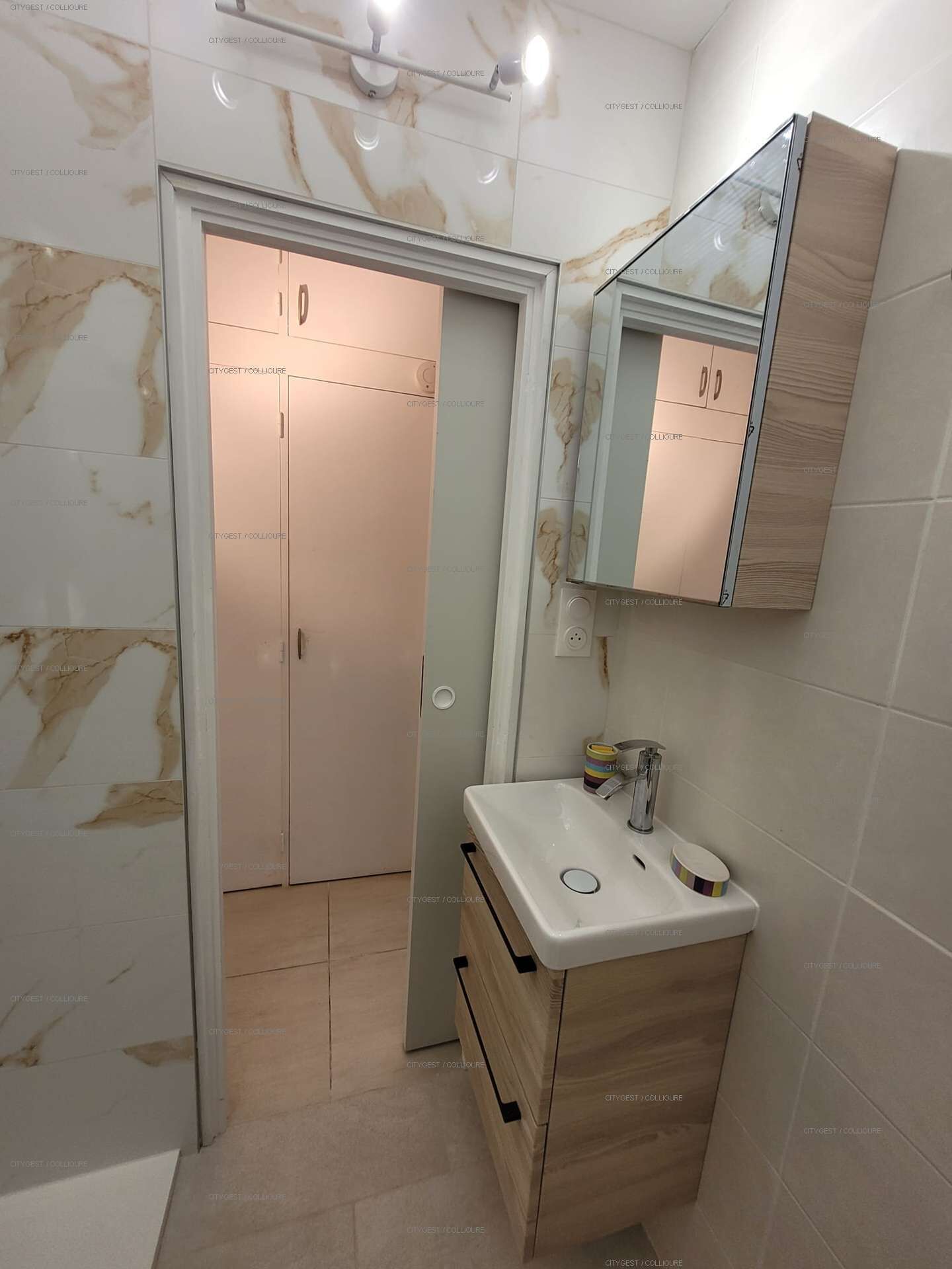 A bathroom with a marble wall, a wooden vanity, a mirror, and a door with a number.
