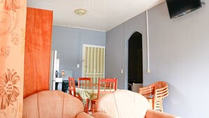 A living room with a sofa, a dining table with chairs, a kitchen area, and a TV mounted on the wall. - Abidager 2  ideal for family with children and groups (Wanica)