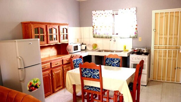 A compact kitchen with wooden cabinets, a refrigerator, a microwave, a stove, and a dining table with chairs. - Abidager 2  ideal for family with children and groups (Wanica)