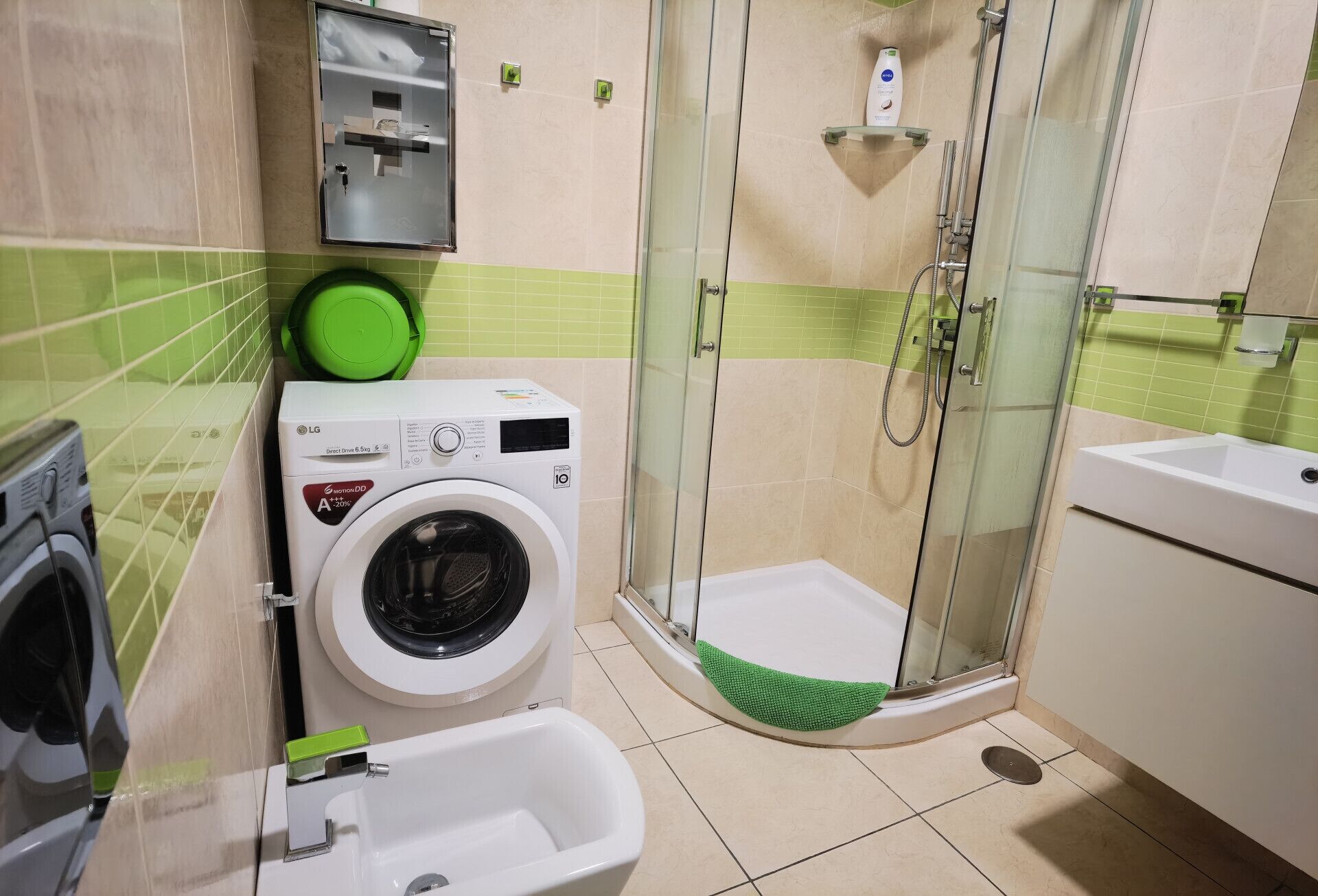 A compact bathroom with a washing machine, a shower, and a sink.