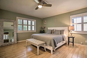 Een slaapkamer met een bed, een bankje, een plafondventilator en grote ramen.