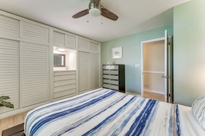 Ein Schlafzimmer mit Bett, Kleiderschrank, Deckenventilator und einer Tür zu einem weiteren Raum.