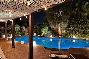 Ein Außenpoolbereich mit einer Pergola, umgeben von Pflanzen und Bäumen.