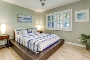 Un dormitorio con cama, lámparas de noche, una ventana con persianas, un cuadro en la pared y una planta en maceta.