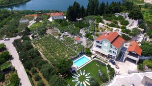 An aerial view of a coastal area with a large body of water, a swimming pool, and several buildings with red roofs. - 5 stars, Family Apartment  Pero at Nature park close to Adriatic sea (Peracko Blato/Ploce)