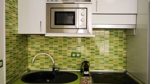 A kitchen with a microwave, sink, and green tiled backsplash. - B124 Seaside view Las Vistas TRG Tenerife Royal Gardens (Playa de la Américas)