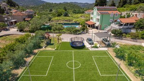 A soccer field with a goalpost, surrounded by houses, a swimming pool, and a green building with solar panels. - Hidden Croatia,  APARTMENT DARIJA, luxury apartment in Nature park (Peracko Blato/Ploce)