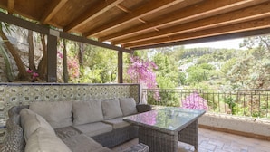 A covered patio with a wicker sofa and glass table, surrounded by a tiled floor and a railing. - CASABRA - Villa with private pool in Urb. Monterrey, Palma de Gandia. Free WiFi (Palma de Gandia)
