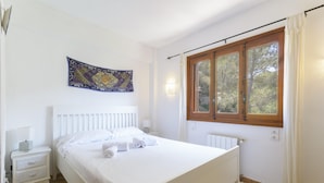 A bedroom with a bed, a nightstand, a wall-mounted tapestry, a window with curtains, and a radiator. - CASABRA - Villa with private pool in Urb. Monterrey, Palma de Gandia. Free WiFi (Palma de Gandia)