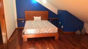 A bedroom with a wooden bed, a nightstand, a wall-mounted shelf, and a sloped ceiling. - Yellow Attic S. Vincent (São Vicente)