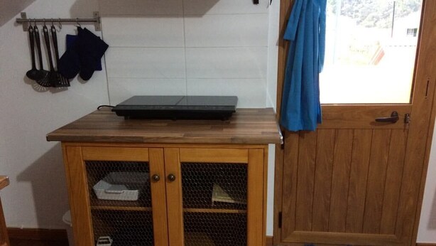 A kitchen with a wooden countertop, a mesh cabinet, and a door with a blue curtain. - Yellow Attic S. Vincent (São Vicente)