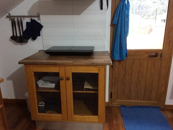 A kitchen with a wooden countertop, a mesh cabinet, and a door with a blue curtain.