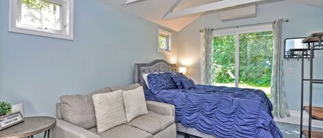 A bedroom with a bed, a sofa, a small table, and a window with curtains.