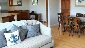 Ein Wohnzimmer mit einer Couch, einem Esstisch mit Stühlen, Holzböden und einer Küche im Hintergrund.