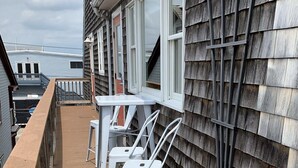Ein Balkon mit Holzboden, weißen Metallstühlen und einem weißen Tisch.