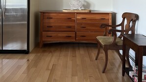 Eine Küche mit Holzschränken, einem Edelstahlkühlschrank, einem Holzesstisch mit Stühlen und einem gerahmten Bild an der Wand.