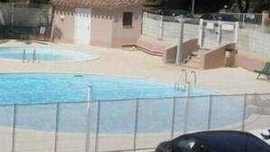 Ein Schwimmbeckenbereich mit zwei Pools, umgeben von einem Zaun, und ein kleines Gebäude mit Tür und Fenstern.