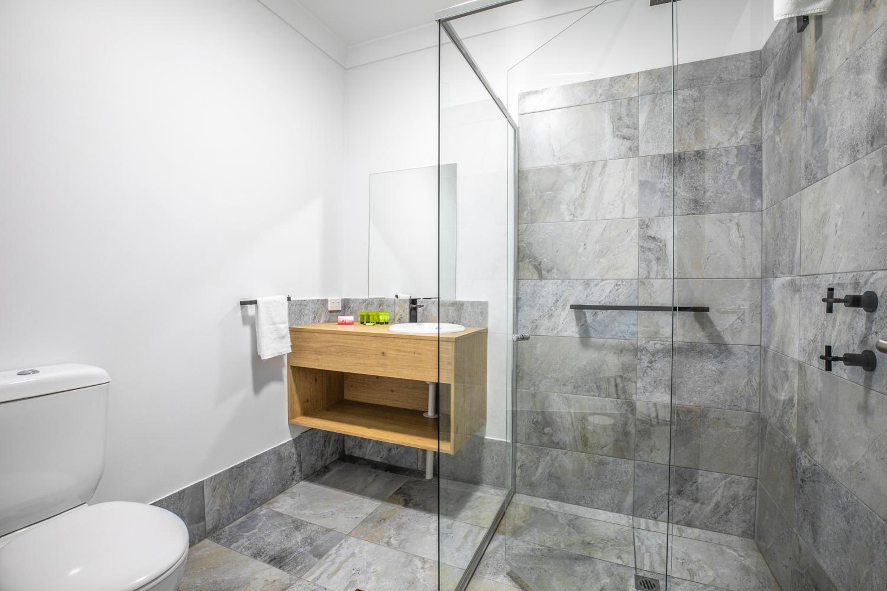 A modern bathroom with a glass shower enclosure, a wooden vanity, and a toilet.