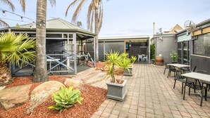 A patio area with outdoor seating, palm trees, and a covered seating area. - Nightcap at Exeter Hotel (Exeter)
