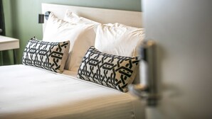 A neatly made bed with white linens and patterned pillows, a bedside table, and a wall-mounted light fixture. - Nightcap at Exeter Hotel (Exeter)
