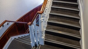 A staircase with wooden balusters and a handrail, carpeted steps, and a white wall with a light fixture. - Nightcap at Exeter Hotel (Exeter)