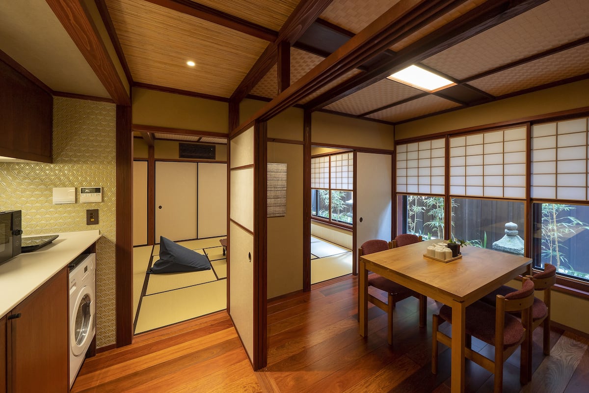 A traditional Japanese room with tatami flooring, a wooden table, and a view of a garden through a shoji screen.