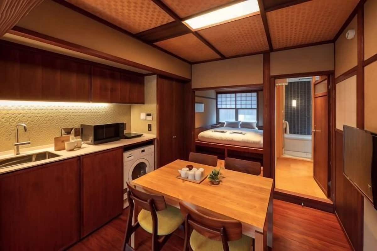 A compact hotel room with a kitchenette, a dining area, a bed, and a view of the outside.