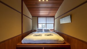 A bedroom with a wooden ceiling, a large window, and a bed with pillows and a blanket. - Utaimachi (Kanazawa)