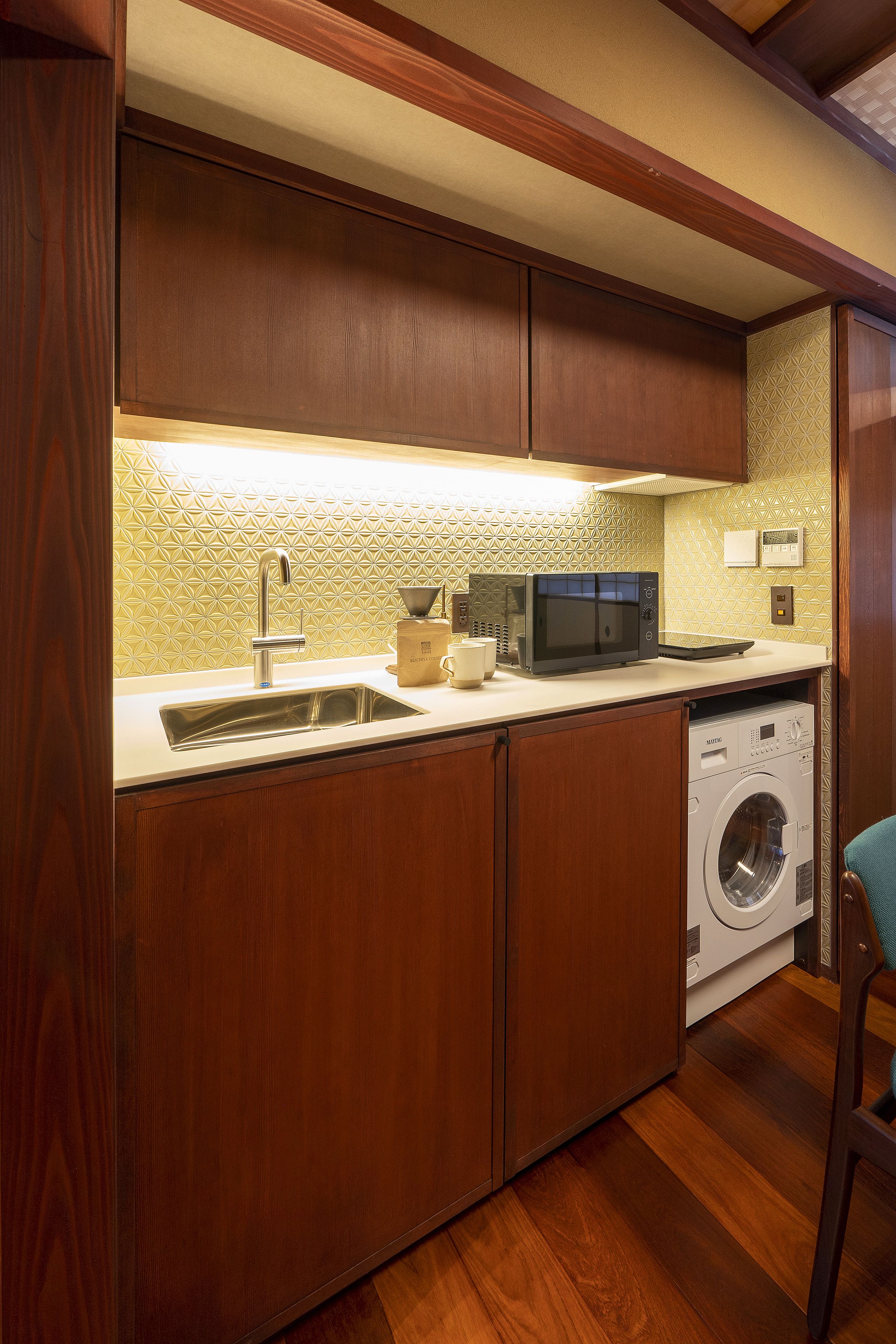 Cocina compacta con armarios de madera, microondas, lavamanos y lavadora.