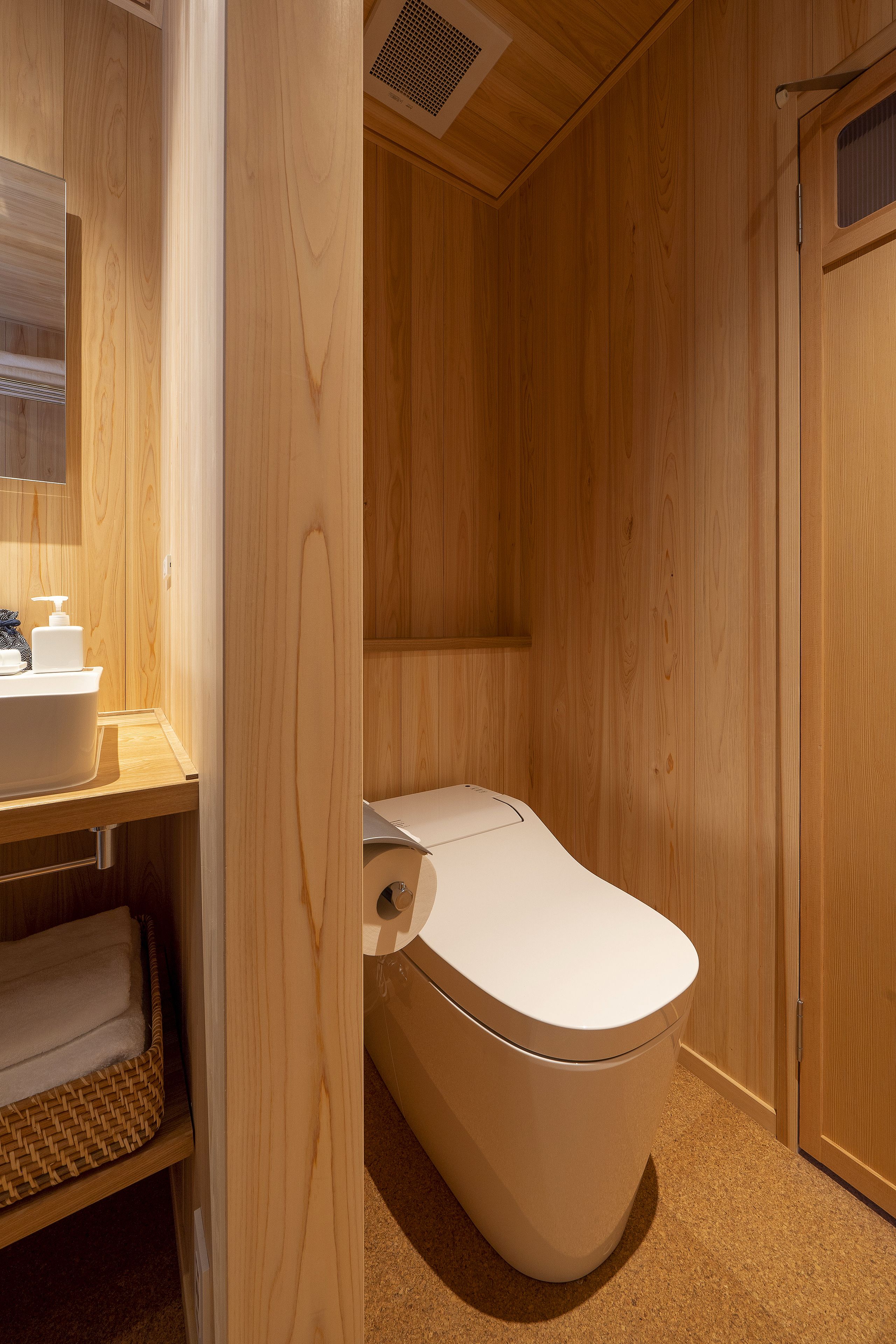 A wooden-paneled bathroom with a white toilet, a sink, and a towel rack.