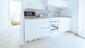 A modern kitchen with white cabinetry, a microwave, an oven, and patterned backsplash tiles.